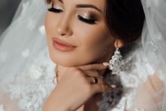 Bride wedding morning. Fashion bride gorgeous beauty, bride woman in robe. Bride touches earrings. Portrait wedding makeup and hairstyle, girl with veil and jewelry at home.
